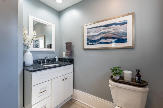 half bathroom with vanity, baseboards, wood finished floors, and toilet