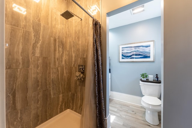 full bathroom featuring toilet, tiled shower, wood finished floors, and baseboards