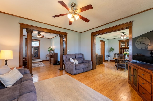 living area with a ceiling fan, light wood-style flooring, crown molding, a baseboard heating unit, and ornate columns