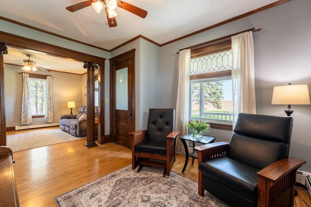 sitting room with a ceiling fan, crown molding, baseboard heating, wood finished floors, and ornate columns