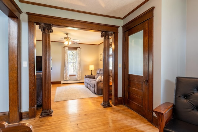 entrance foyer with ornamental molding, ornate columns, light wood finished floors, baseboard heating, and a ceiling fan