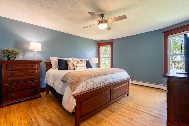 bedroom with baseboard heating, a textured ceiling, light wood-style floors, a ceiling fan, and baseboards