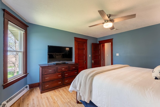 bedroom featuring a baseboard radiator, light wood-style flooring, baseboards, and a ceiling fan