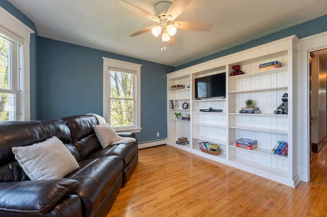 living area with baseboard heating, light wood finished floors, a ceiling fan, and healthy amount of natural light