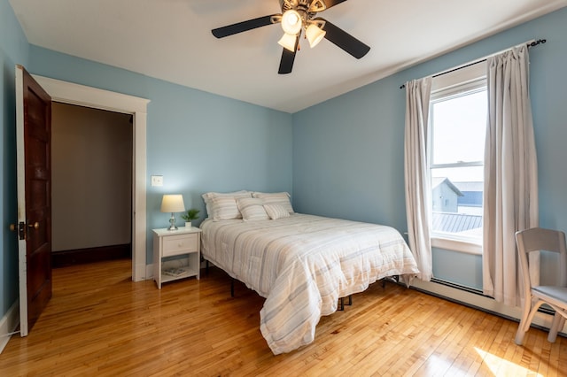 bedroom featuring light wood finished floors, ceiling fan, baseboards, and baseboard heating