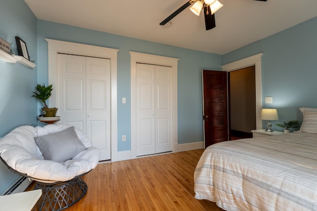 bedroom with two closets, light wood-style flooring, baseboards, and ceiling fan
