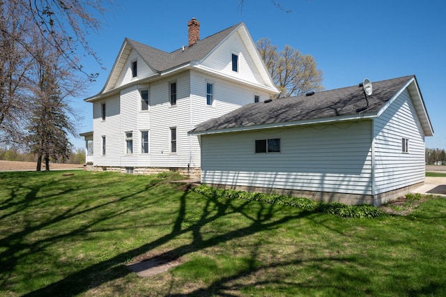view of side of home featuring a chimney, a yard, and roof with shingles