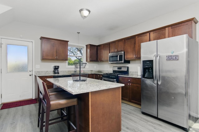 kitchen with appliances with stainless steel finishes, light wood-style floors, a kitchen island, light stone counters, and a breakfast bar