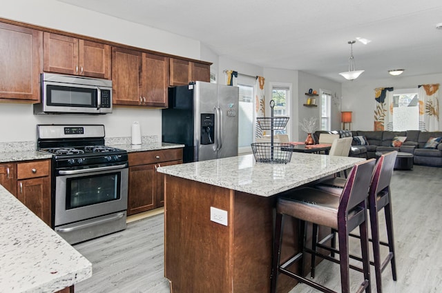 kitchen featuring appliances with stainless steel finishes, light wood-type flooring, a breakfast bar area, and light stone countertops