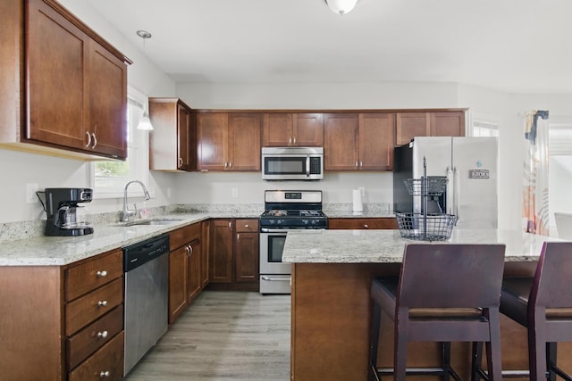 kitchen featuring appliances with stainless steel finishes, a sink, light wood-type flooring, a kitchen breakfast bar, and a kitchen island