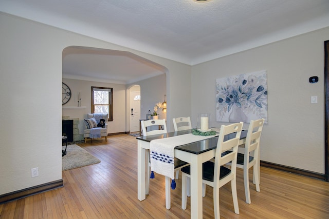 dining room with arched walkways, light wood finished floors, baseboards, and a tiled fireplace