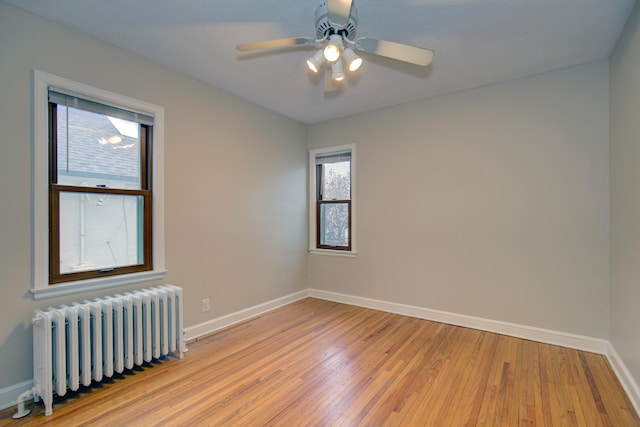 spare room with radiator, light wood-style flooring, baseboards, and a ceiling fan