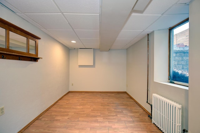 basement with radiator, a drop ceiling, light wood-style floors, baseboards, and recessed lighting