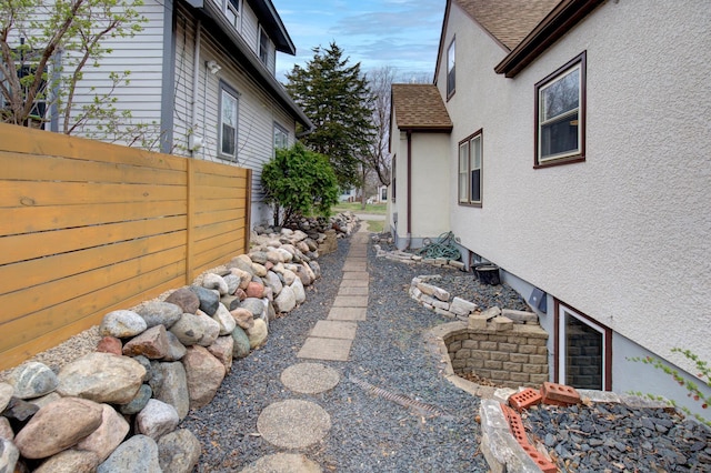 view of side of home featuring fence, stucco siding, and roof with shingles