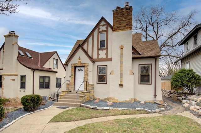 english style home featuring stucco siding, a shingled roof, a chimney, and entry steps