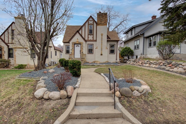 tudor house with a chimney, a shingled roof, stucco siding, and a front lawn