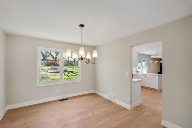 unfurnished dining area featuring a chandelier, light wood-type flooring, and baseboards