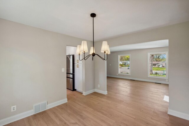 unfurnished dining area with a chandelier, light wood-style flooring, and baseboards