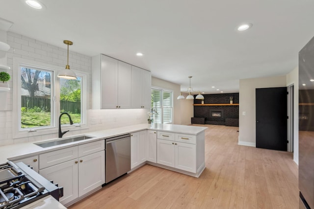 kitchen featuring dishwasher, a sink, a brick fireplace, white cabinetry, and recessed lighting