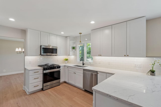 kitchen with appliances with stainless steel finishes, a sink, open shelves, light stone counters, and light wood-type flooring