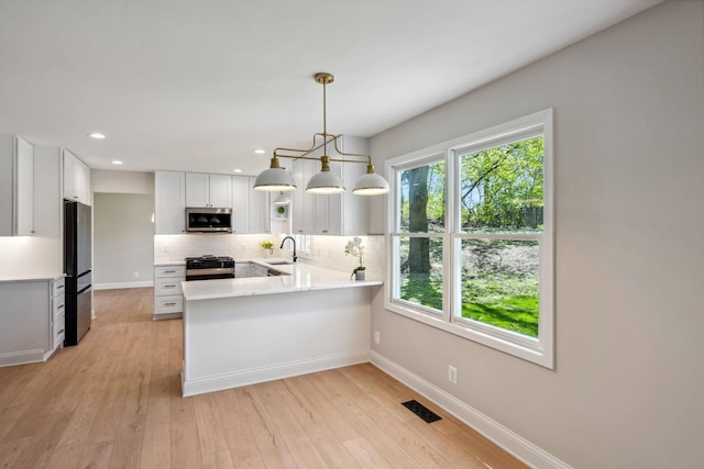 kitchen featuring appliances with stainless steel finishes, a sink, backsplash, a peninsula, and light countertops