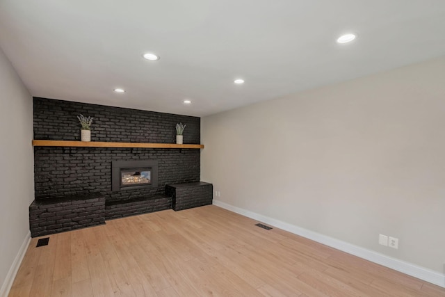 unfurnished living room with baseboards, a brick fireplace, wood finished floors, and recessed lighting