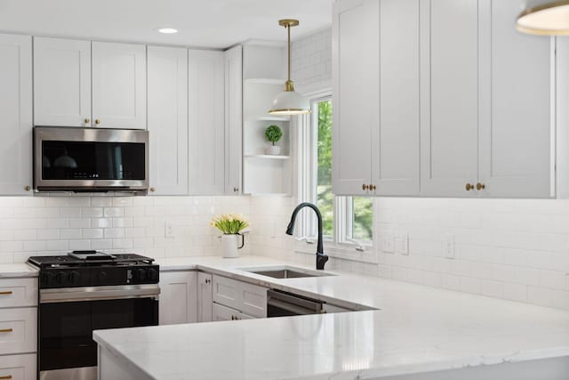 kitchen featuring stainless steel microwave, range with gas stovetop, a sink, white cabinets, and light stone counters
