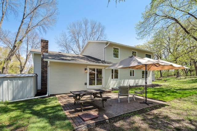rear view of house with a chimney, a storage shed, a patio area, a lawn, and an outbuilding