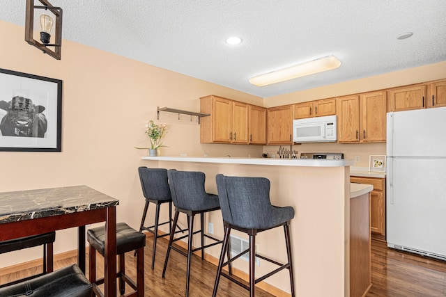 kitchen featuring a textured ceiling, a kitchen breakfast bar, white appliances, and wood finished floors