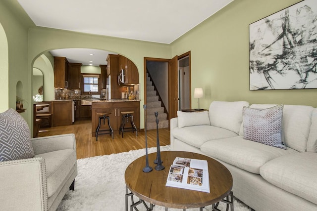living room featuring arched walkways, light wood-type flooring, and stairway
