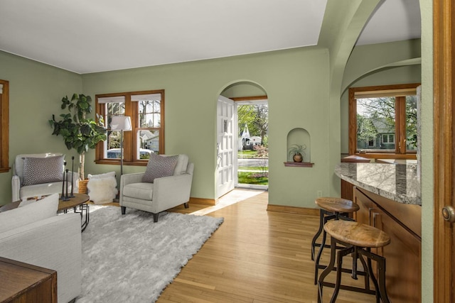 living area with light wood-type flooring, baseboards, and arched walkways
