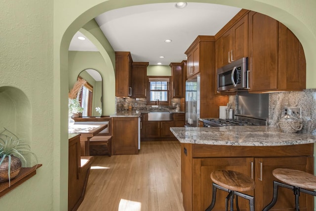 kitchen featuring appliances with stainless steel finishes, a sink, a peninsula, decorative backsplash, and light wood-style flooring