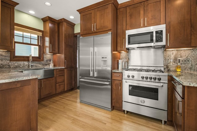 kitchen featuring high end appliances, a sink, backsplash, light stone countertops, and recessed lighting