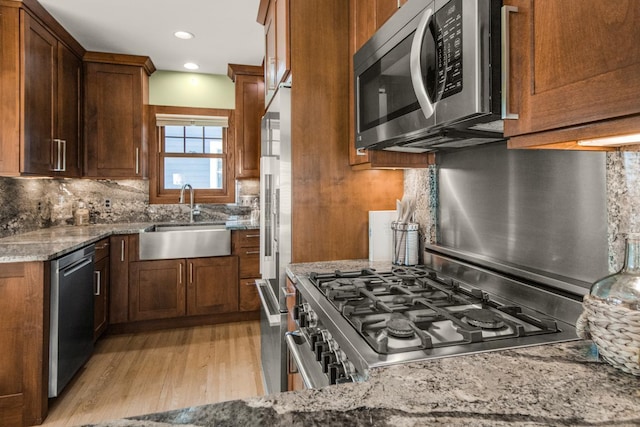 kitchen featuring stainless steel appliances, a sink, tasteful backsplash, light stone counters, and light wood finished floors