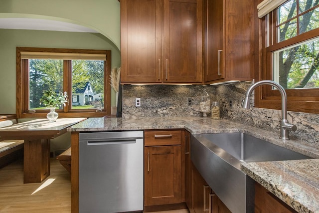 kitchen with stainless steel dishwasher, a sink, light stone counters, and decorative backsplash