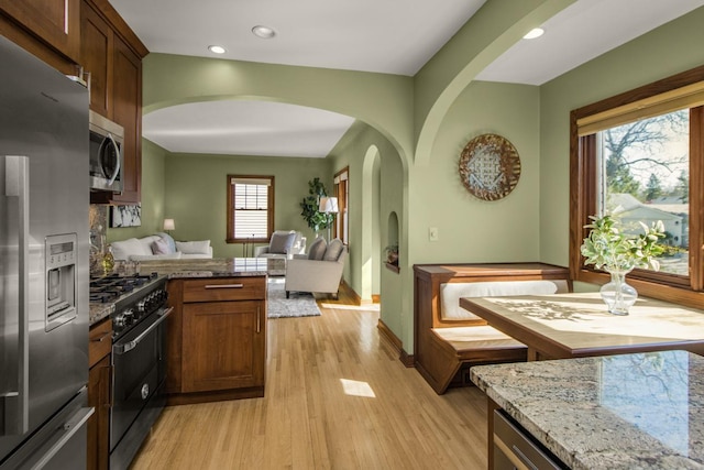 kitchen with appliances with stainless steel finishes, open floor plan, light wood finished floors, a peninsula, and arched walkways