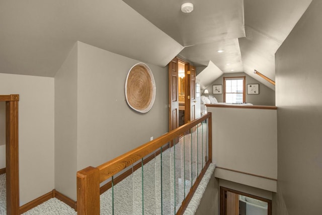 hallway with an upstairs landing, lofted ceiling, carpet floors, and baseboards