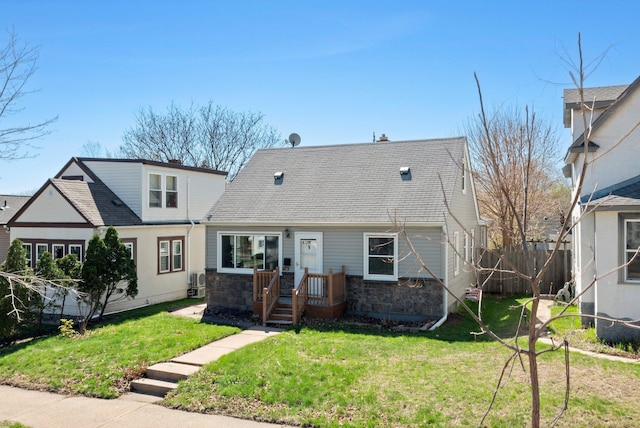 view of front of property featuring stone siding, fence, a shingled roof, and a front yard