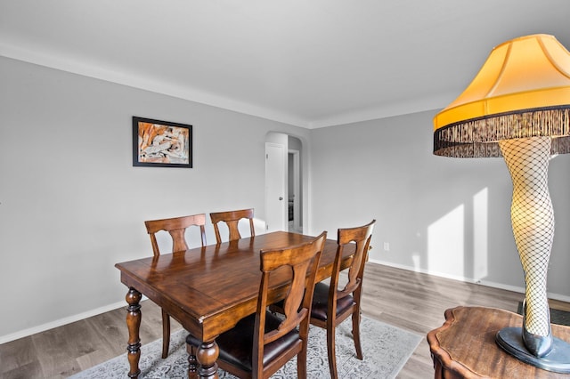 dining area featuring arched walkways, baseboards, and wood finished floors