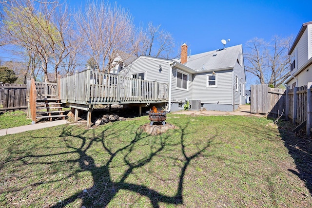 back of house featuring a chimney, a lawn, a deck, a fenced backyard, and a fire pit