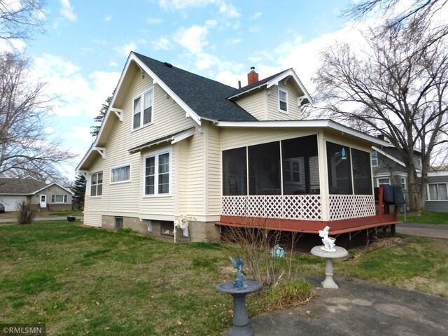 view of side of property featuring a sunroom, a shingled roof, a lawn, and a chimney