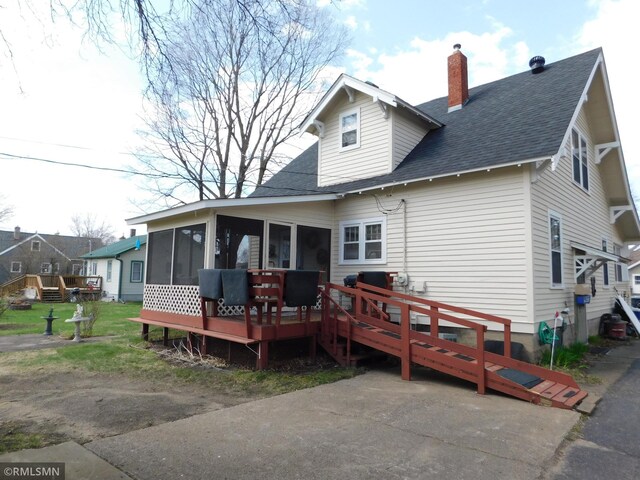 rear view of house featuring a wooden deck, a shingled roof, a sunroom, and a chimney