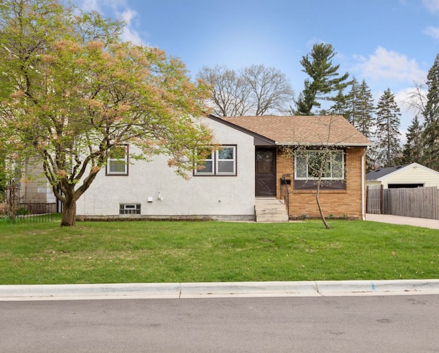 view of front of house featuring a front lawn, a shingled roof, brick siding, and fence