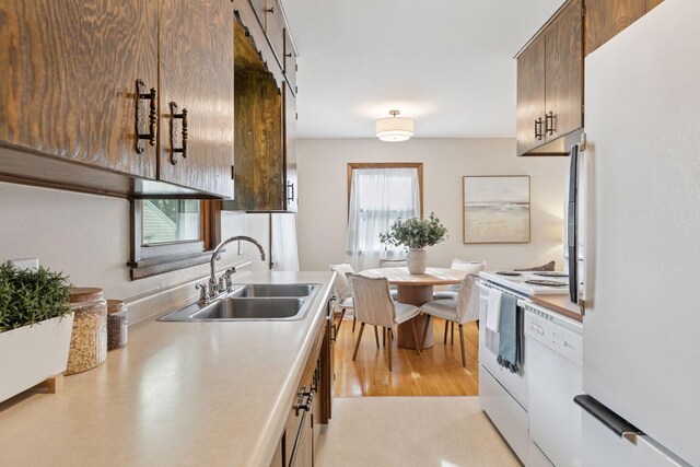 kitchen with light countertops, light wood-style flooring, a sink, and white appliances