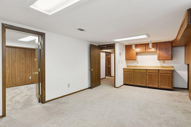 kitchen with light colored carpet, visible vents, brown cabinetry, and baseboards