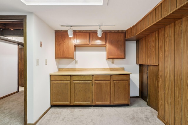 kitchen with track lighting, light countertops, light carpet, and brown cabinetry