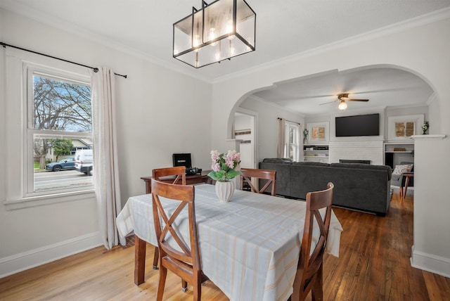 dining space with a ceiling fan, crown molding, arched walkways, wood finished floors, and baseboards