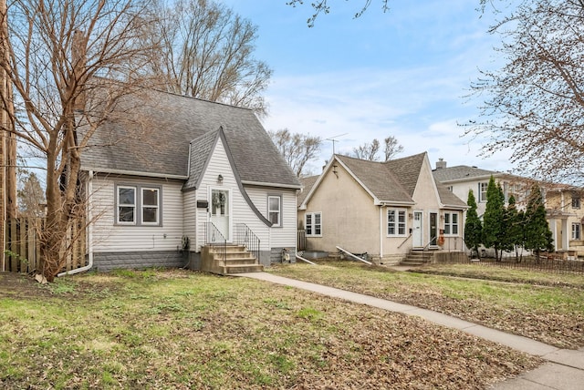 view of front of property featuring fence, roof with shingles, and a front lawn