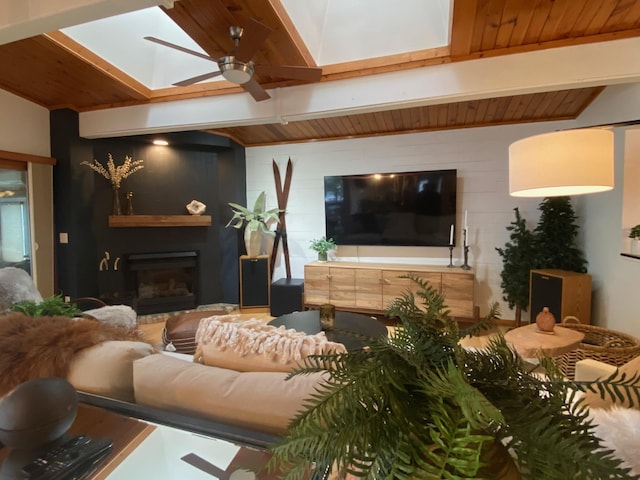 living area with a skylight, a ceiling fan, a glass covered fireplace, and beam ceiling
