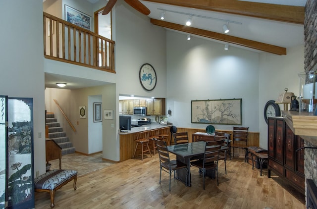 dining space with track lighting, stairs, a towering ceiling, beam ceiling, and light wood-style flooring